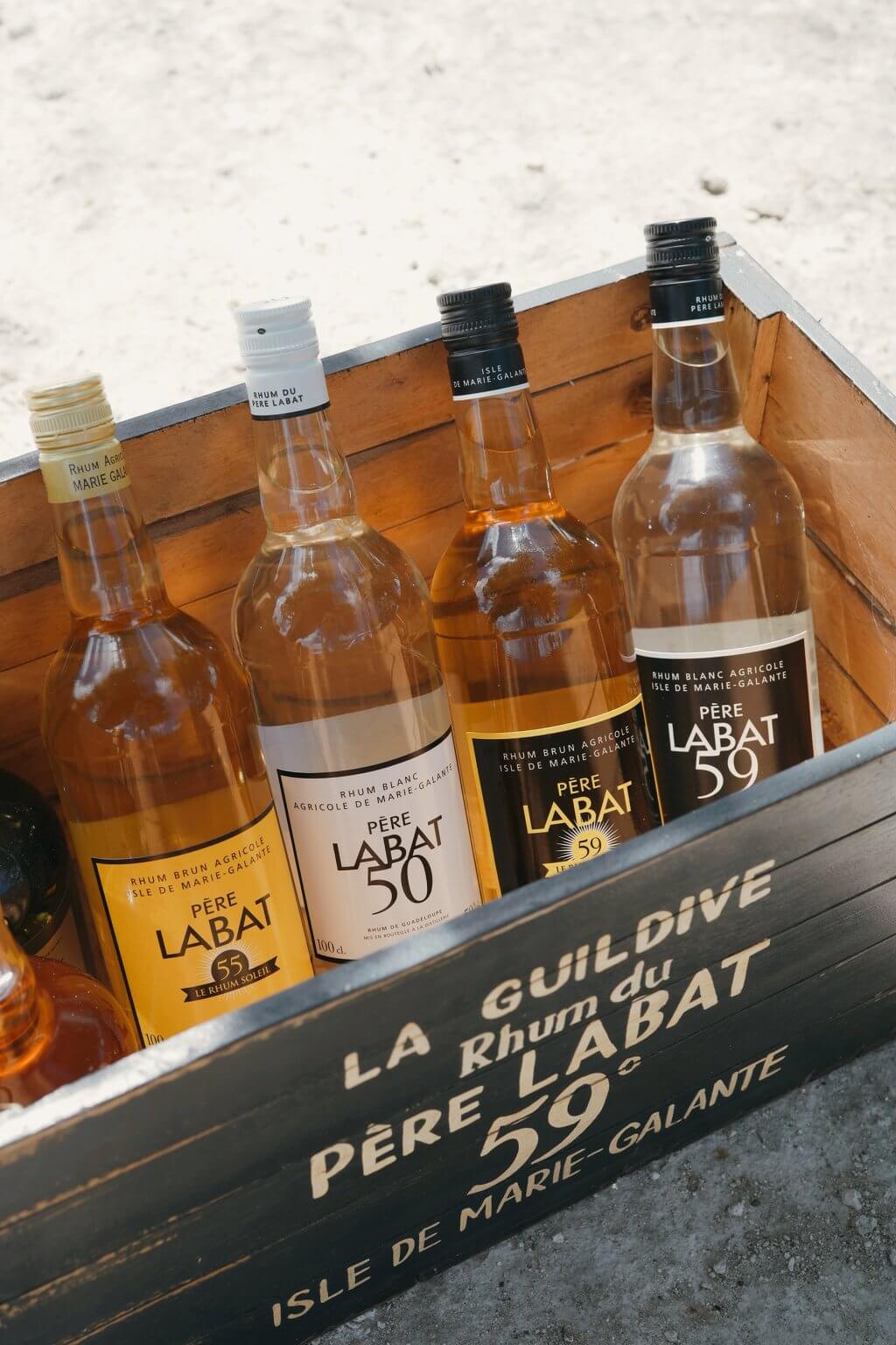 Caisse La Guildive Père Labat vue de dessus avec bouteilles 55, 50 et 59 sur le sable
